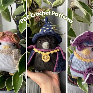 Op de afbeelding: Drie gehaakte amigurumi-pinguïn speelgoedjes. De eerste pinguïn draagt een roze hoed met bruine beschermbrillen en een beige sjaal. De tweede pinguïn draagt een paarse en blauwe tovenaarshoed en een paarse en gouden mantel. De derde pinguïn draagt een paarse en blauwe piratenhoed met een paarse ooglap en een paarse en blauwe sjerp.