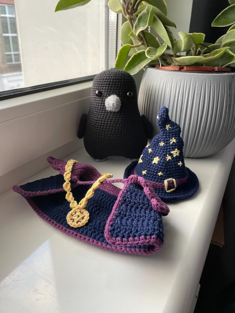 May include: A crocheted black bird with a white beak, a blue and purple crocheted robe with a gold chain, and a blue crocheted hat with yellow stars.