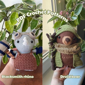 May include: Two crocheted amigurumi figures: a blacksmith rhino and a druid bear. The rhino is gray, brown, and blue, holding a hammer. The bear is brown and green, wearing a hooded cloak and holding a staff. The text "PDF Crochet Patterns" is visible.