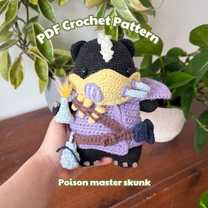Könnte beinhalten: Handgefertigte gehäkelte Poison Master Skunk Puppe. Der Skunk ist schwarz, weiß und gelb, trägt eine lila Weste und trägt einen hellblauen Gegenstand. Der Text "PDF Crochet Pattern" steht oben und "Poison master skunk" unten.