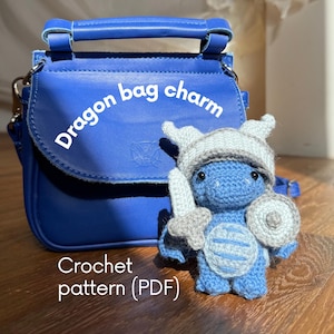 May include: A blue leather handbag with a top handle and a crochet dragon bag charm featuring a light blue helmet, sword, and shield. The text "Dragon bag charm" and "Crochet pattern (PDF)" is visible on the image.