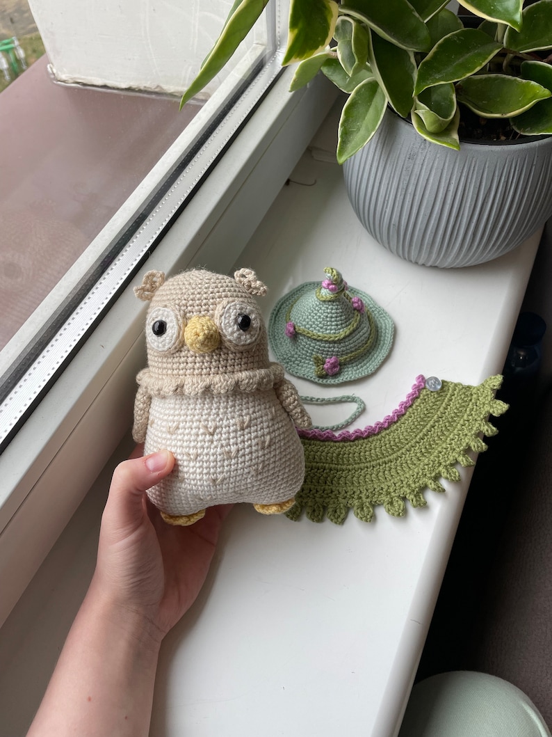 May include: A crocheted owl with brown and white yarn, a green crocheted hat with pink flowers, and a green crocheted collar with pink trim.