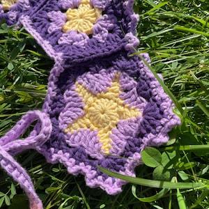 May include: A crocheted flower garland with purple and yellow flowers. The garland is made of yarn and has a scalloped edge.
