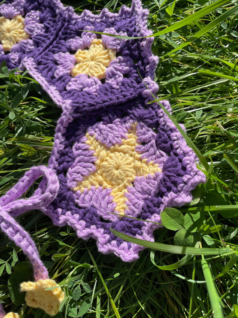 May include: A crocheted flower garland with purple and yellow flowers. The garland is made of yarn and has a scalloped edge.