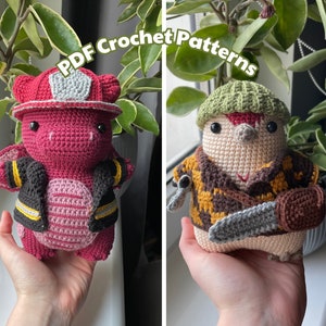 May include: Two crocheted amigurumi toys. The first is a red dragon wearing a firefighter's hat and jacket. The second is a beige creature wearing a green hat and a brown plaid shirt with a chainsaw.