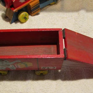 May include: A red wooden toy train car with a removable top and an elephant illustration on the side. The car has four wheels and is made of wood.