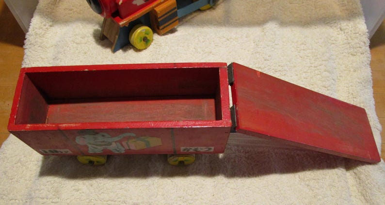 May include: A red wooden toy train car with a removable top and an elephant illustration on the side. The car has four wheels and is made of wood.