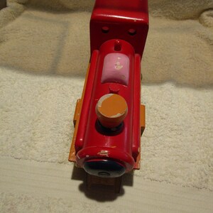 May include: A red wooden toy train engine with a pink and orange painted detail. The engine has a black painted wheel and a black painted face.
