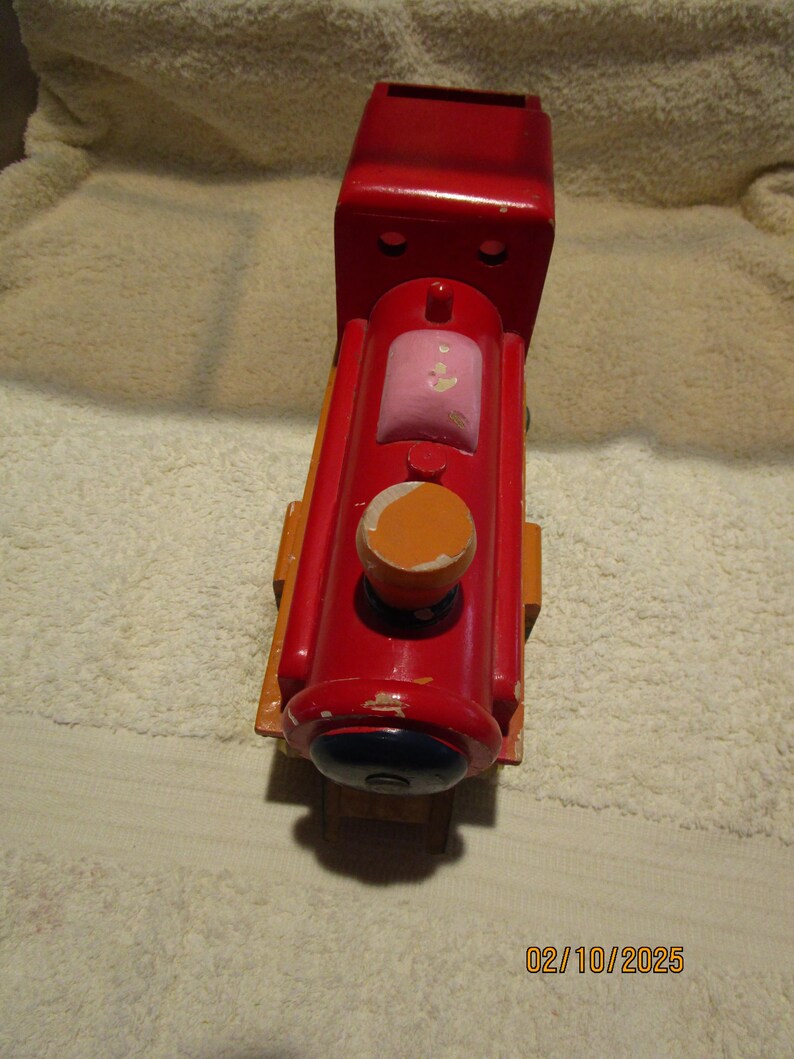May include: A red wooden toy train engine with a pink and orange painted detail. The engine has a black painted wheel and a black painted face.