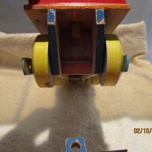 May include: A wooden toy truck with yellow wheels and blue accents. The truck is red and has a wooden bed.