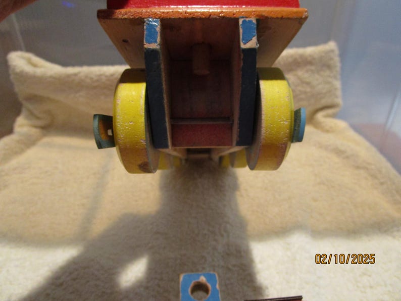 May include: A wooden toy truck with yellow wheels and blue accents. The truck is red and has a wooden bed.