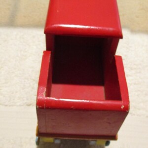 May include: A red wooden toy train engine with a pink and brown cab. The engine has a removable top and a yellow and green base.