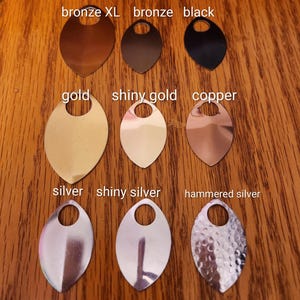 May include: A collection of metal scales in various colors, including bronze, black, gold, copper, and silver. The scales are oval-shaped with a hole at the top for attachment. The text on the image indicates the color of each scale.