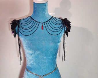 May include: Black shoulder armour with layered chain accents and a red crystal pendant. The armour features scale-like shoulder pads and long chain dangles. A gold-coloured chain belt is also visible.