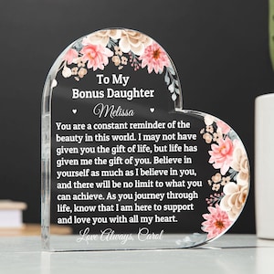 May include: A heart-shaped acrylic keepsake with floral accents and the text "To My Bonus Daughter Melissa." The clear piece has a heartfelt message and is a decorative gift.