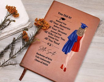 May include: A brown leather-bound notebook with the text "You Did It!" and a graduation-themed illustration. The notebook includes the graduate's name, degree, university, and class year. A bookmark is attached.