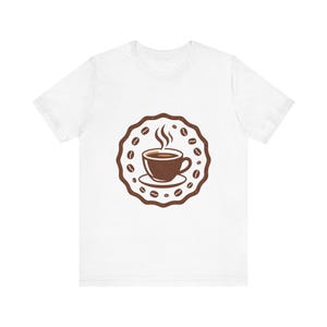 May include: White t-shirt with a brown coffee cup design, steam rising from the cup, surrounded by coffee beans in a circular frame. The design is centered, offering a casual and comfortable look.