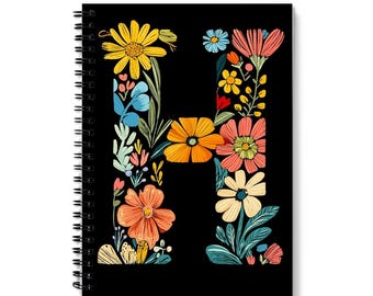 May include: A black spiral notebook with a floral design forming the letter "H". The flowers are in shades of pink, yellow, orange, blue, and green.