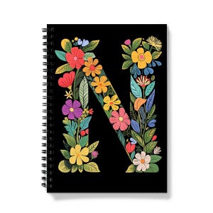 Könnte beinhalten: Ein schwarzes Spiralnotizbuch mit einem bunten Blumenmuster, das den Buchstaben N bildet. Die Blumen sind in den Farben Pink, Gelb, Blau, Grün und Rot.