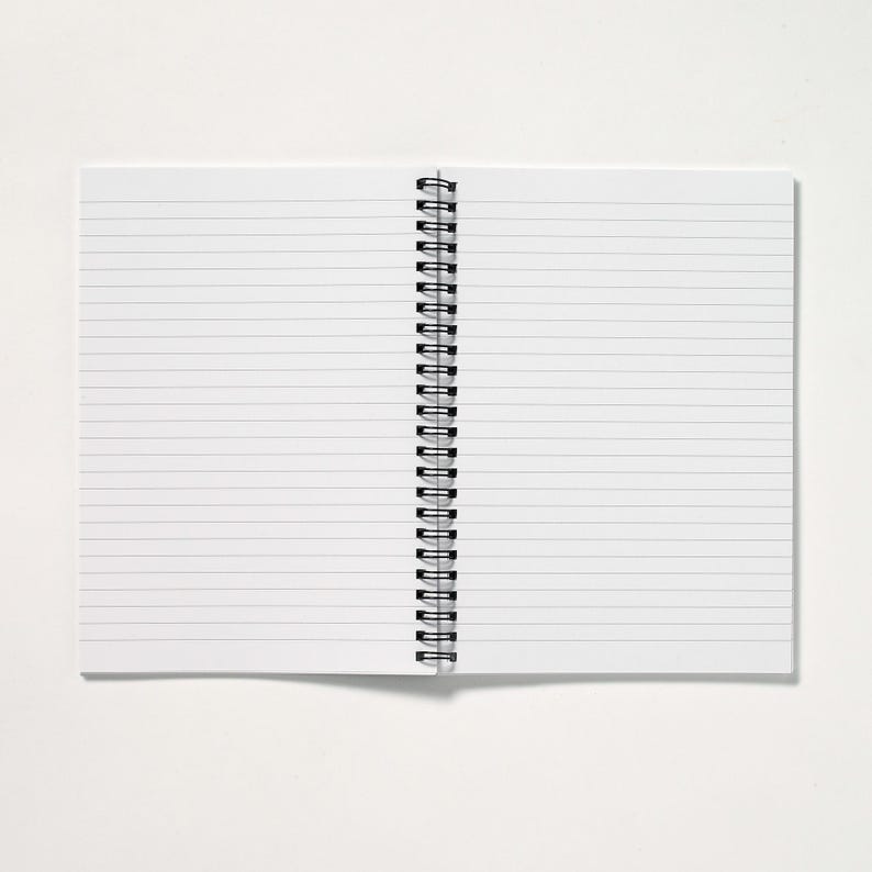May include: An open, lined notebook with a black spiral binding. The pages are white with horizontal gray lines. The notebook is on a white surface.