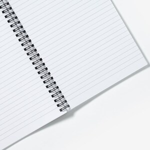 May include: A white, spiral-bound notebook with lined pages. The black metal spiral binding runs along the left edge. The notebook is open, displaying the interior pages with horizontal lines.