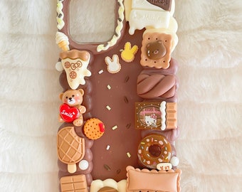 May include: A brown phone case decorated with various dessert-themed charms. The case features a chocolate bar design with a variety of miniature sweets, including a teddy bear, ice cream, and a donut. The case has a clear camera cutout.