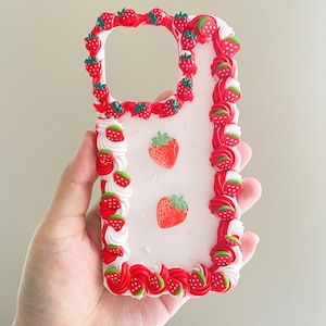May include: A white phone case with a red and white frosting design and strawberry decorations.