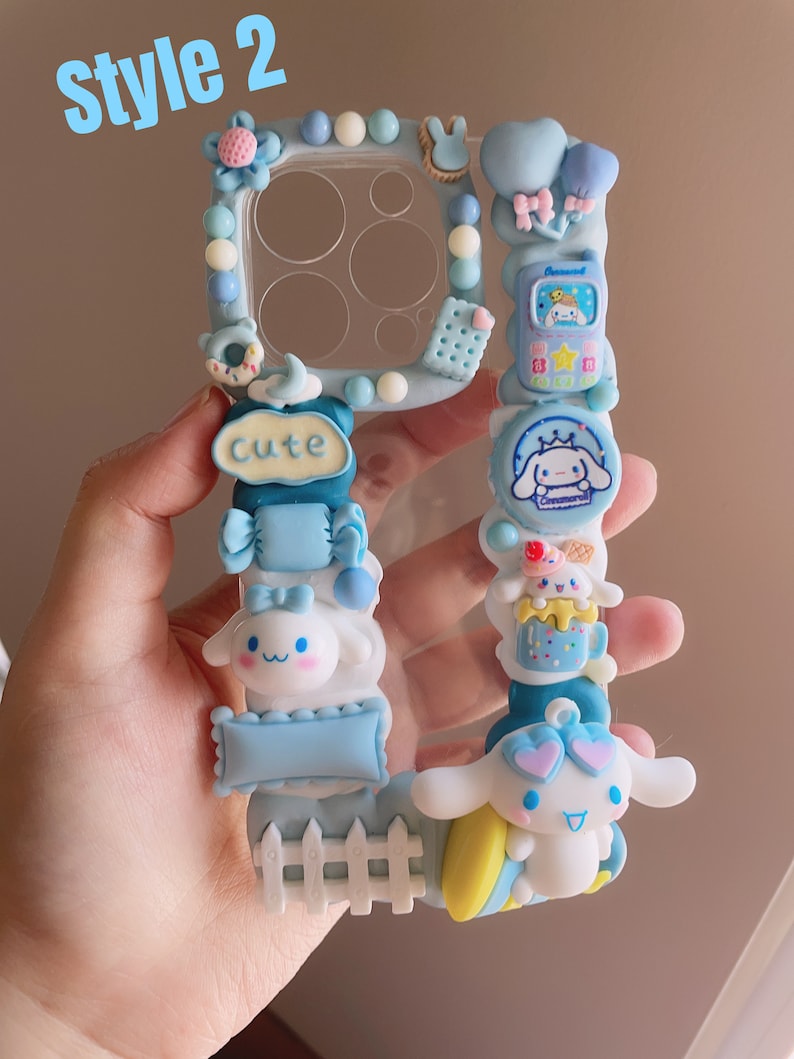 May include: A blue and white phone case decorated with a variety of 3D charms, including a small white dog with a pink bow, a blue and white candy cane, a blue and white fence, and a blue and white sign that says "Cute".
