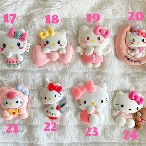 May include: A set of 10 Hello Kitty charms, each featuring a different design. The charms are made of pink, white and yellow plastic and are approximately 5 cm tall. The charms are numbered 17 through 24.