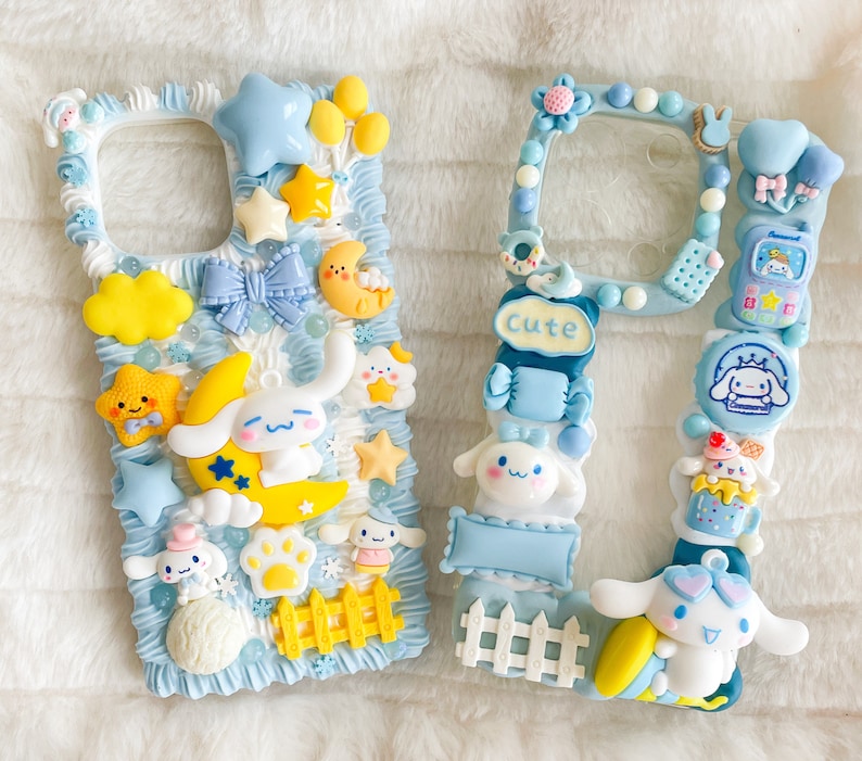 May include: Two white phone cases decorated with pastel blue, yellow, and pink 3D embellishments. The cases feature cartoon characters, hearts, stars, and the word "Cute".