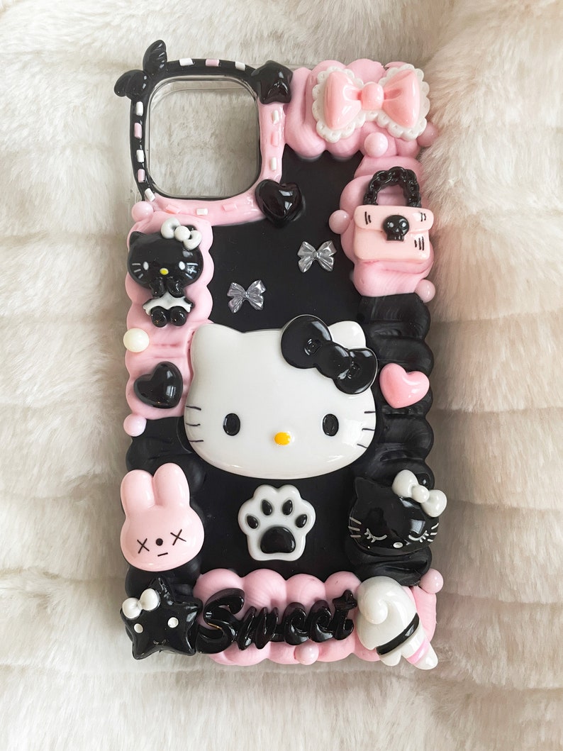 May include: Black and pink phone case featuring Hello Kitty, a bunny, a cat, and a paw print. The case has a pink and white bow, a pink purse, and the word "Sweet" written on it.