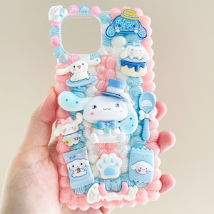 May include: A pink and blue phone case with a 3D design featuring a cartoon dog character with a blue hat and bow tie. The case is decorated with various other 3D elements, including a cupcake, a spoon, and a paw print.