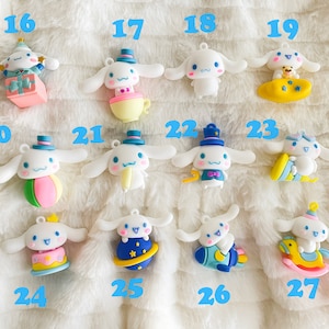 May include: A collection of 12 white plush dog charms with different colored accessories. The charms are numbered 16 through 27. Each charm features a different design, including a birthday cake, a ball, a teacup, a rocket, a rocking horse, and a planet.