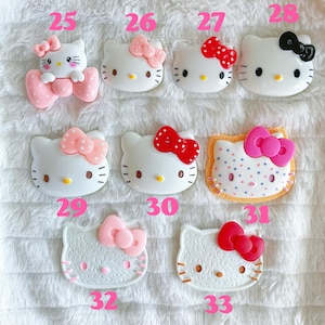 May include: A collection of 10 Hello Kitty themed resin charms. The charms are in various colours and designs, including pink, red, white, and black. Some charms feature Hello Kitty's face, while others feature her full body. The charms are numbered 25 through 33.