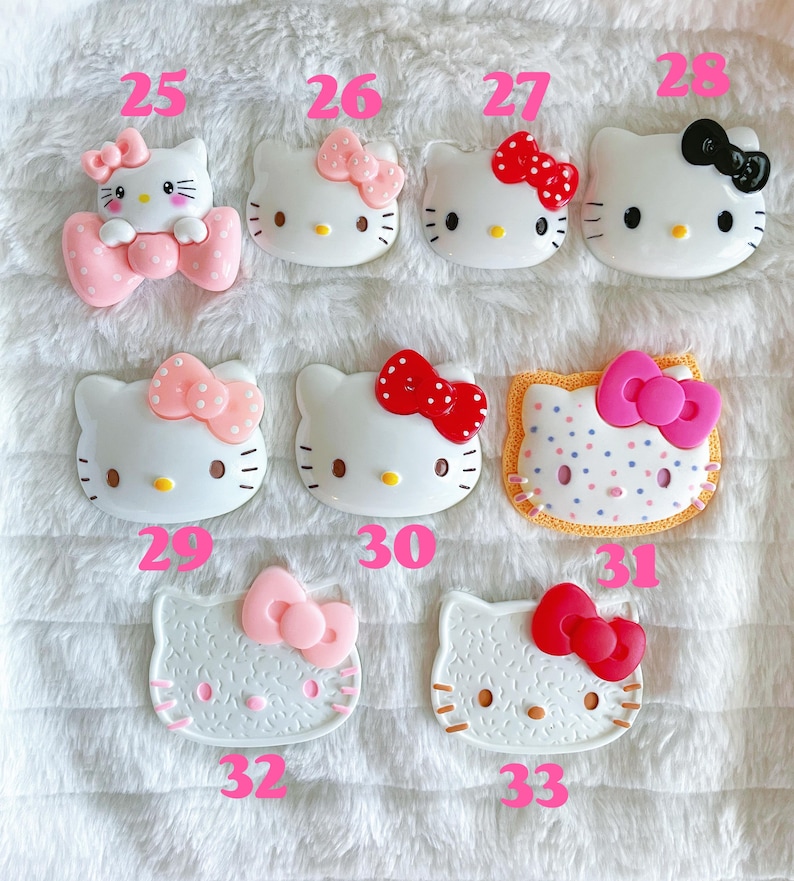 May include: A collection of 10 Hello Kitty themed resin charms. The charms are in various colours and designs, including pink, red, white, and black. Some charms feature Hello Kitty's face, while others feature her full body. The charms are numbered 25 through 33.