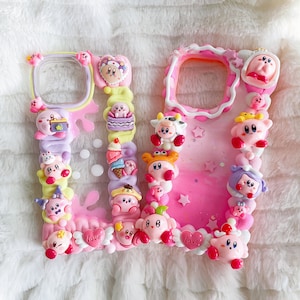 Peut inclure: Une coque de téléphone rose et blanche décorée de divers personnages 3D colorés, dont une vache rose et blanche, un personnage rose et jaune avec une couronne et un personnage rose et blanc avec un chapeau. La coque présente également des cœurs roses et blancs, des étoiles et le mot "love".