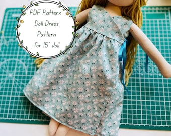 Peut inclure: Une robe de poupée en tissu bleu clair avec un motif floral blanc et rose. La robe présente un corsage croisé et un ruban bleu sur le côté. Le texte sur l'image indique : PDF Pattern Doll Dress Pattern for 15" doll.