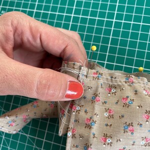 May include: Close-up of fabric with a floral pattern in pink and blue on a tan background. Yellow pins secure the fabric edges. The fabric is being sewn, showcasing a sewing project.