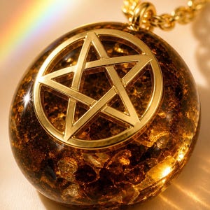 Pode incluir: Um pingente redondo com um símbolo de pentagrama em tom dourado incrustado numa esfera de resina translúcida de cor âmbar, preenchida com pequenas escamas douradas refletoras. O pingente está preso a um colar de corrente de metal dourado.
