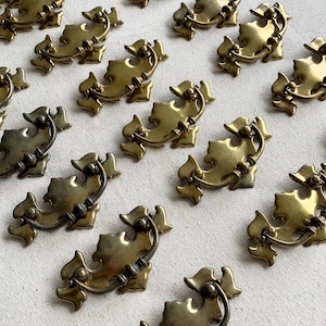 May include: A selection of antique brass drawer pulls. Each pull has a decorative, stylized design with a curved handle. The pulls are arranged on a neutral surface, highlighting their aged, golden finish. These hardware pieces are suitable for vintage furniture restoration.