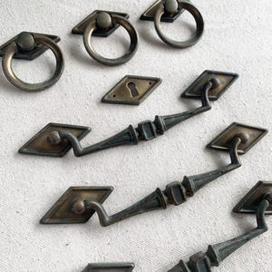 Peut inclure: Ensemble de quincaillerie en laiton antique comprenant des poignées à anneau, des plaques arrière en forme de losange et des tirettes de tiroir décoratives. Le laiton vieilli présente une finition ternie, idéale pour la restauration de meubles anciens.