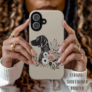May include: A beige phone case with a black and white illustration of a German Shorthaired Pointer dog with pink and white flowers. The dog's name, "Ruby", is written in cursive on the case.