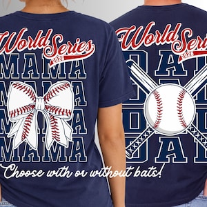 May include: A navy blue t-shirt featuring the text World Series 2026 in red and white. One version displays a white baseball-themed bow, while the other shows a white baseball with crossed bats. The word MAMA is printed in large white block letters.