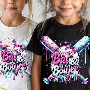 May include: Two children wearing t-shirts with a graphic design of crossed baseball bats and a baseball with the text "Bat & Boujee" in pink and blue dripping paint. The design is on a white t-shirt and a black t-shirt.