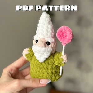 Könnte beinhalten: Häkelanleitung für einen Gnome, der einen rosa Lolli hält. Der Gnome trägt ein grünes Hemd und eine weiße Mütze. Die Anleitung ist als PDF-Download verfügbar.