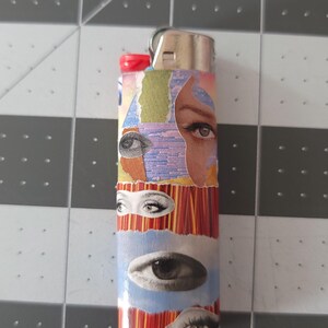 May include: A silver lighter with a colorful collage of eyes on the side. The collage features a variety of colors, including blue, red, yellow, and green.