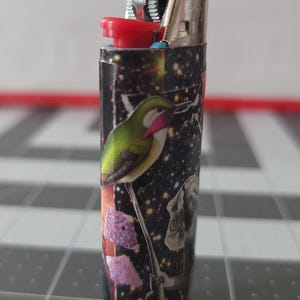 May include: A black lighter with a colorful design featuring a hummingbird, flowers, and a galaxy-like background.