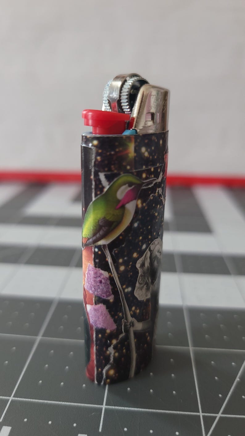 May include: A black lighter with a colorful design featuring a hummingbird, flowers, and a galaxy-like background.