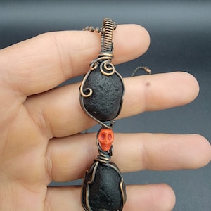 May include: A copper wire wrapped pendant featuring two black stones and a small orange skull bead.