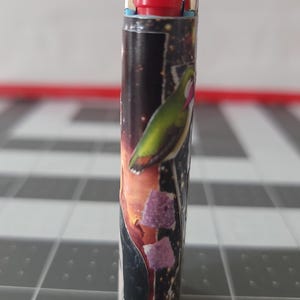 May include: A silver lighter with a red top and a colorful design featuring a bird and a galaxy-like background.